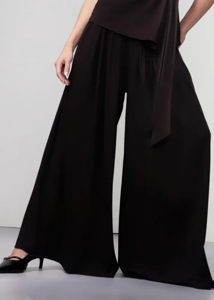 Person wearing a black outfit with wide-leg pants on a plain background