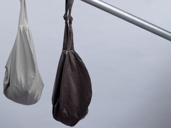 Three slouchy shoulder bags in black, off-white, and dark brown hang from a silver metal rod against a light gray background.