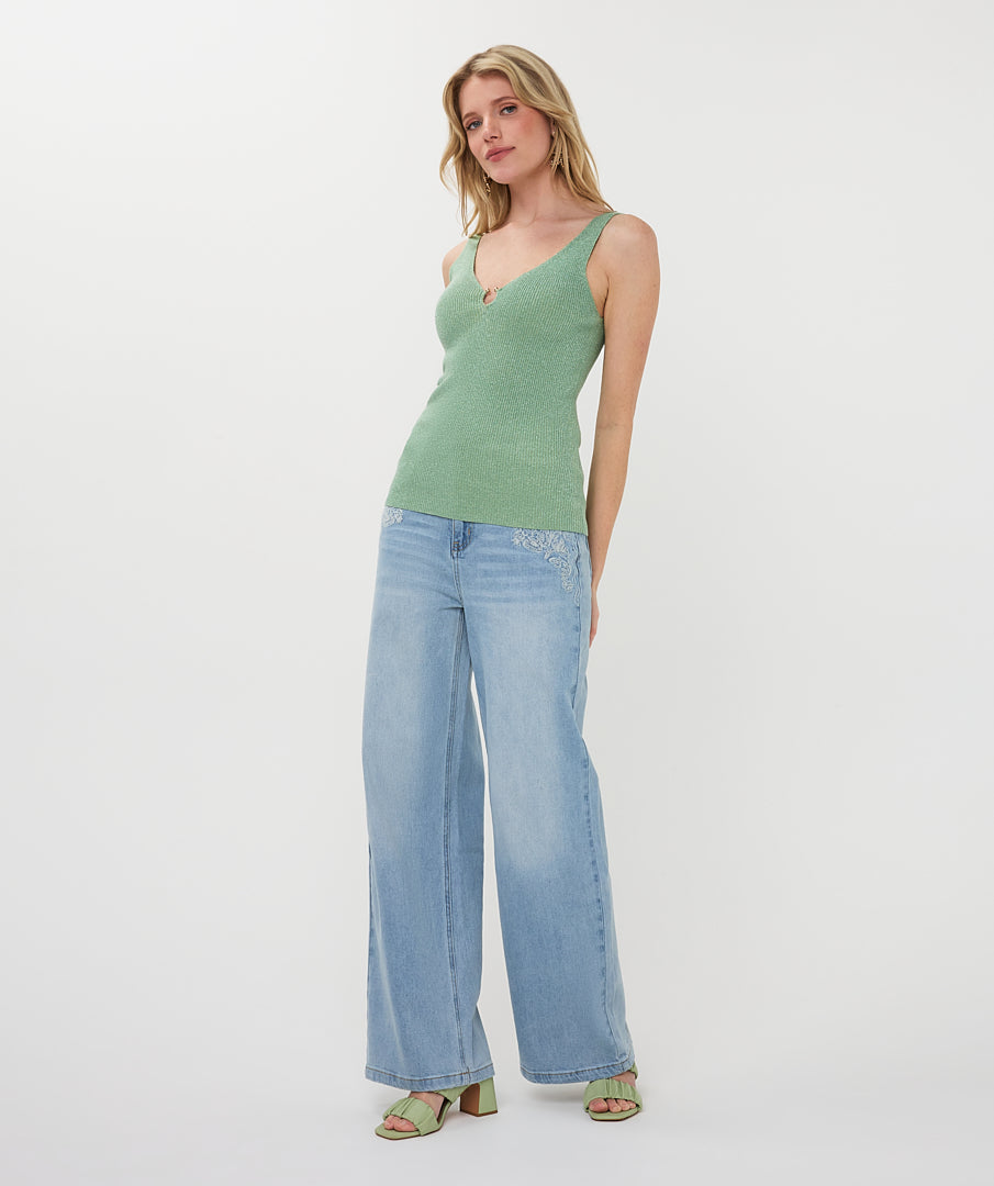 Woman wearing a green tank top and light blue jeans on a white background
