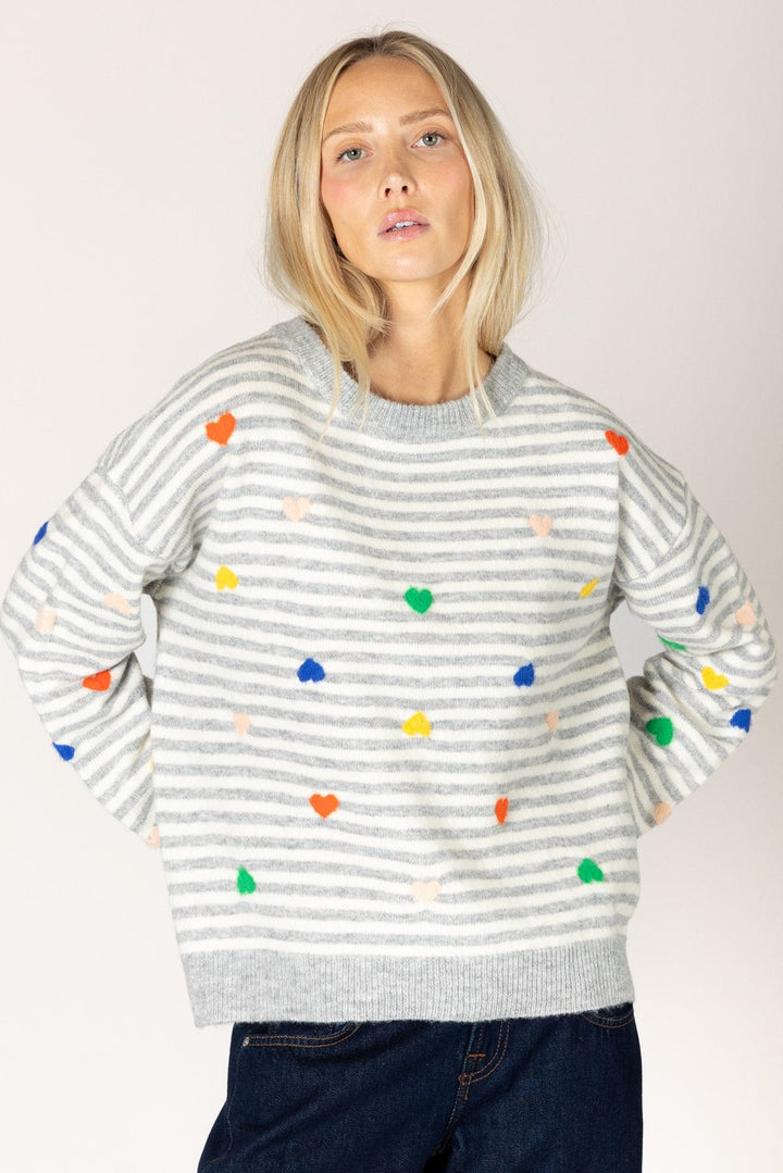 Woman wearing a striped sweater with colorful heart patterns on a plain background