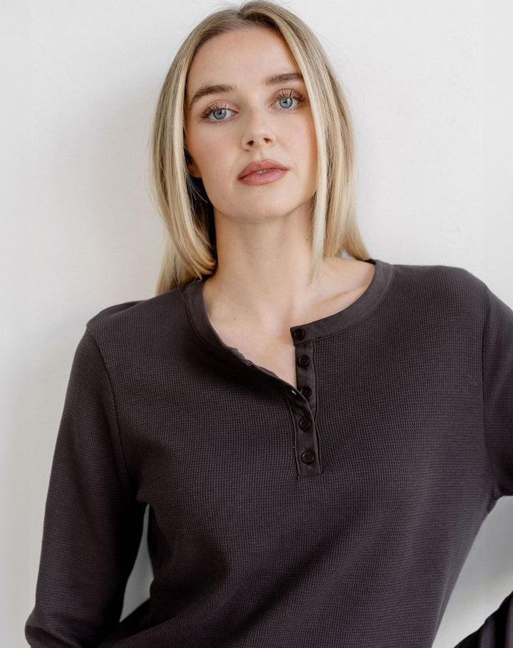A blonde woman wearing a dark brown waffle-knit long-sleeve henley top with a three-button placket, photographed against a plain off-white background.