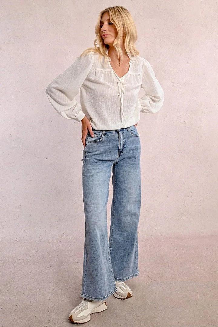 Woman wearing a white blouse and blue jeans against a plain background