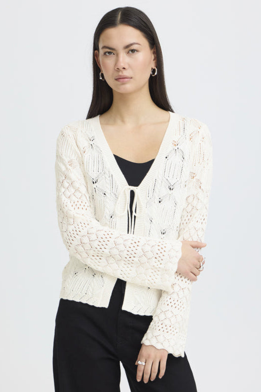 Woman wearing a white lace cardigan over a black top on a light gray background