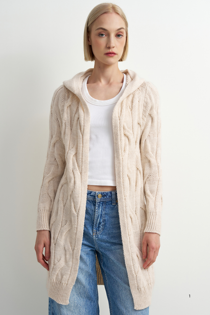 A woman modeling a long cream cable-knit hooded cardigan over a white top and blue jeans, photographed against a plain light background.