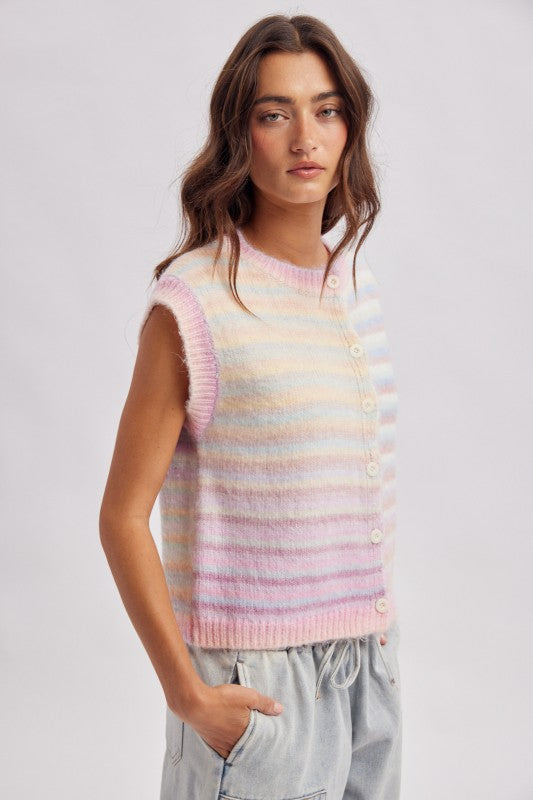 A woman wearing a sleeveless, button-front knit vest with pastel horizontal stripes in pink, yellow, blue, and white, paired with light gray drawstring pants, against a light gray studio background.