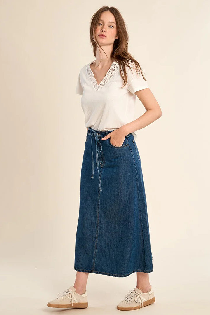 Woman wearing a white top and blue denim skirt on a beige background