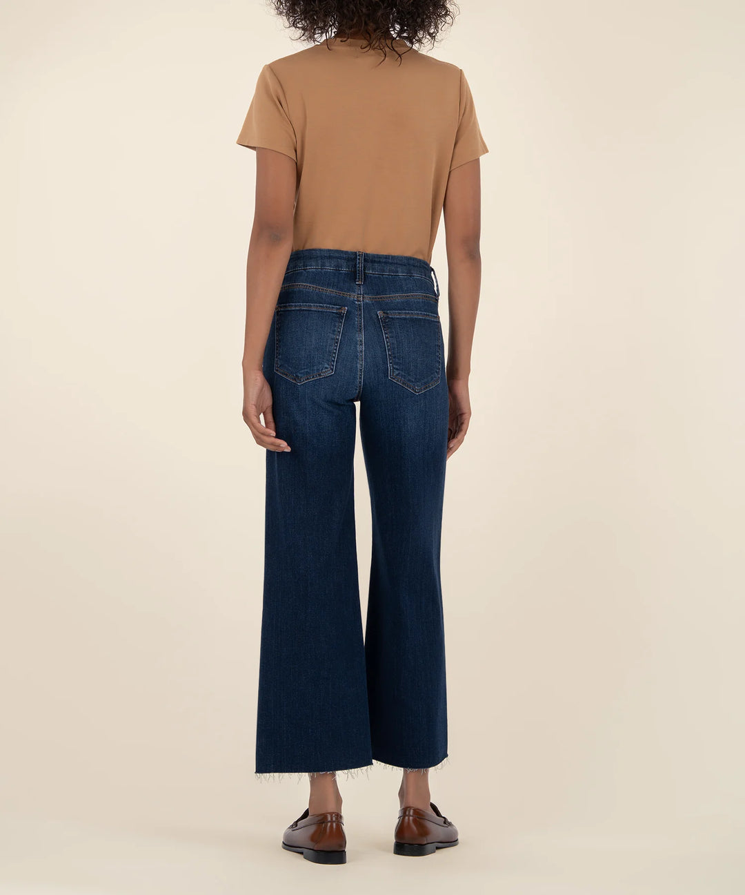 Person wearing a tan t-shirt and dark blue jeans on a beige background