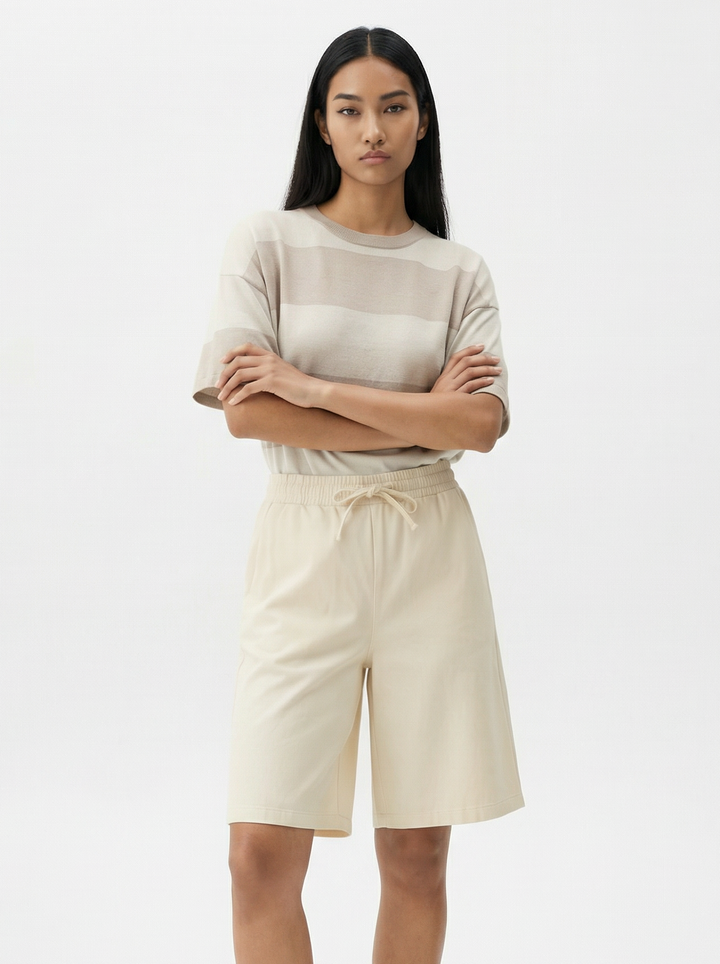 Woman wearing a light-colored top and beige shorts on a white background