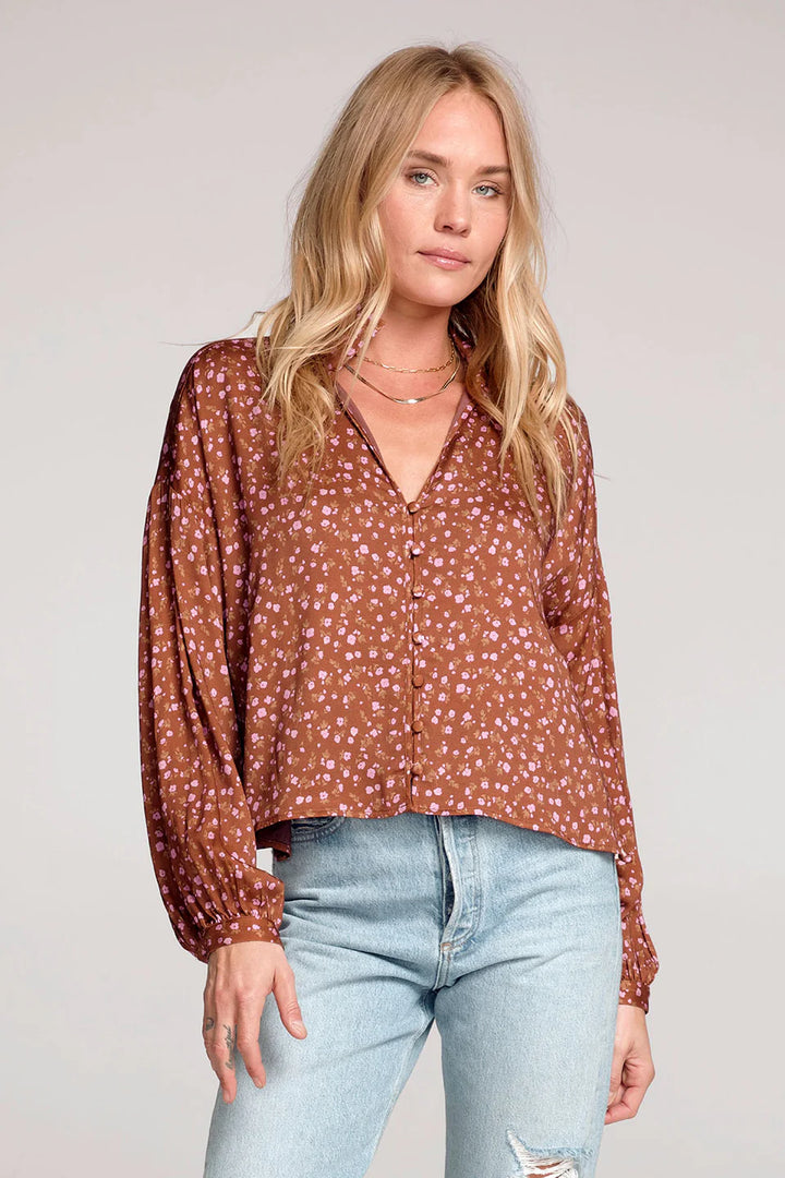 Woman wearing a brown floral blouse and light blue jeans against a plain background
