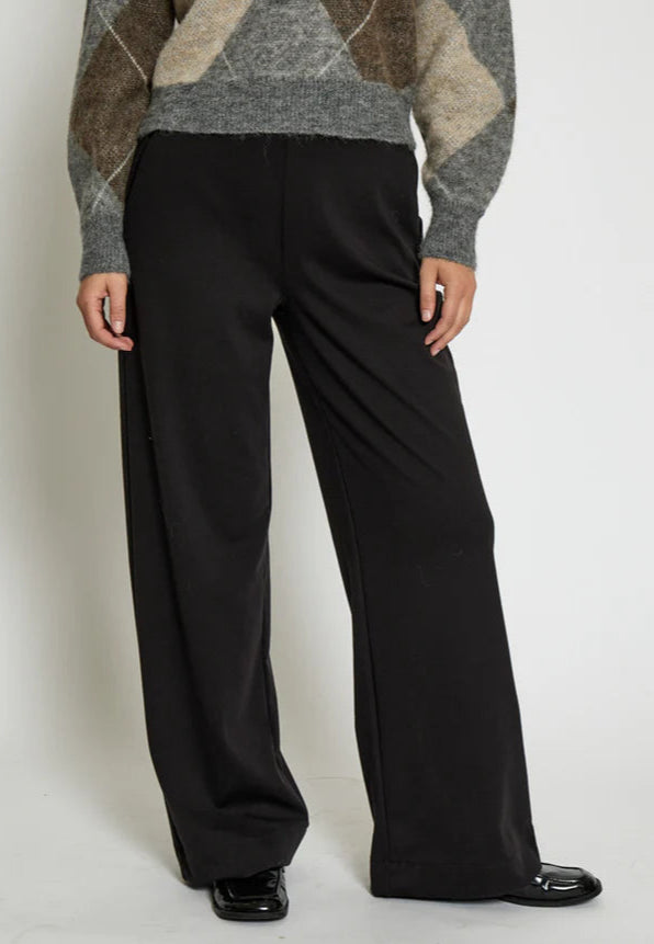 Person wearing a patterned sweater and black pants on a white background