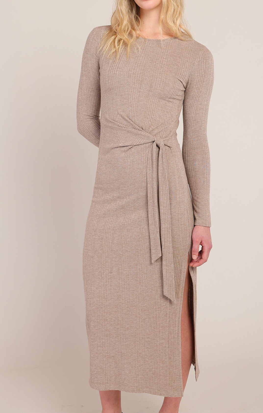 Woman wearing a long brown dress with a belt on a beige background