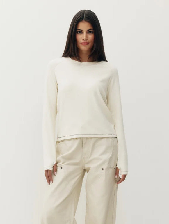 A woman modeling a cream-colored two-piece knit set consisting of a long-sleeve top and matching wide-leg trousers, paired with tan slip-on shoes, against a plain white studio background.