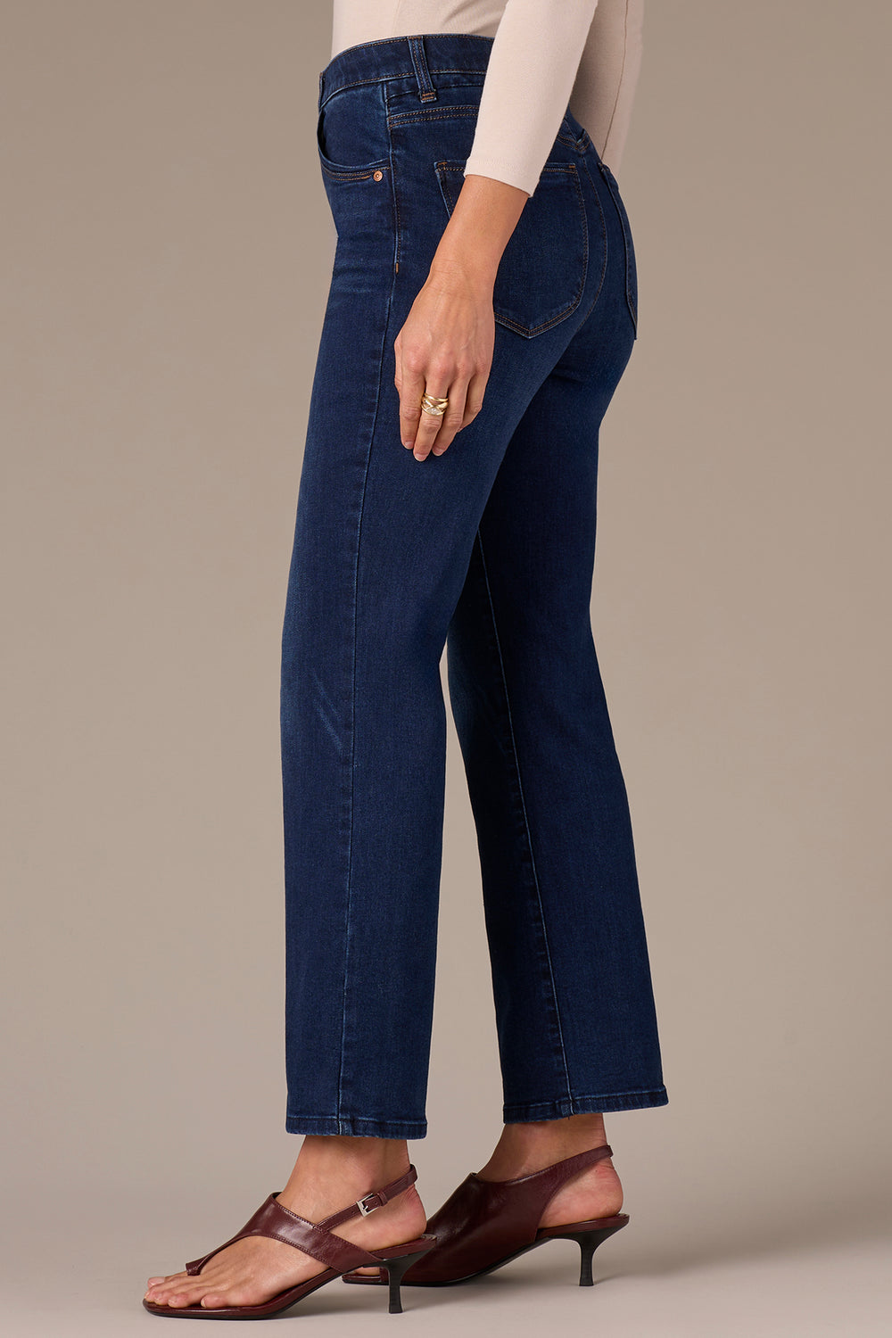 Person wearing dark blue jeans on a neutral background