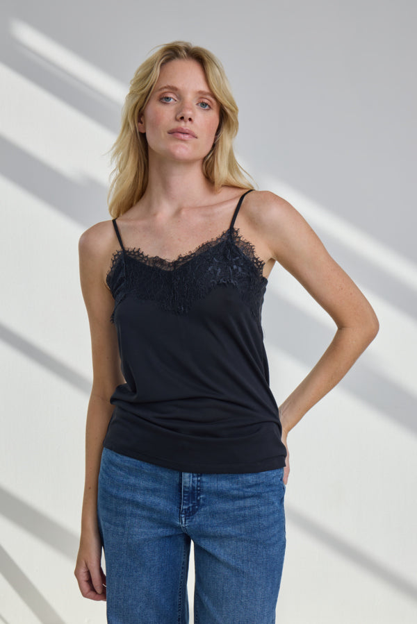 Woman wearing a black lace-trimmed tank top and blue jeans against a white background