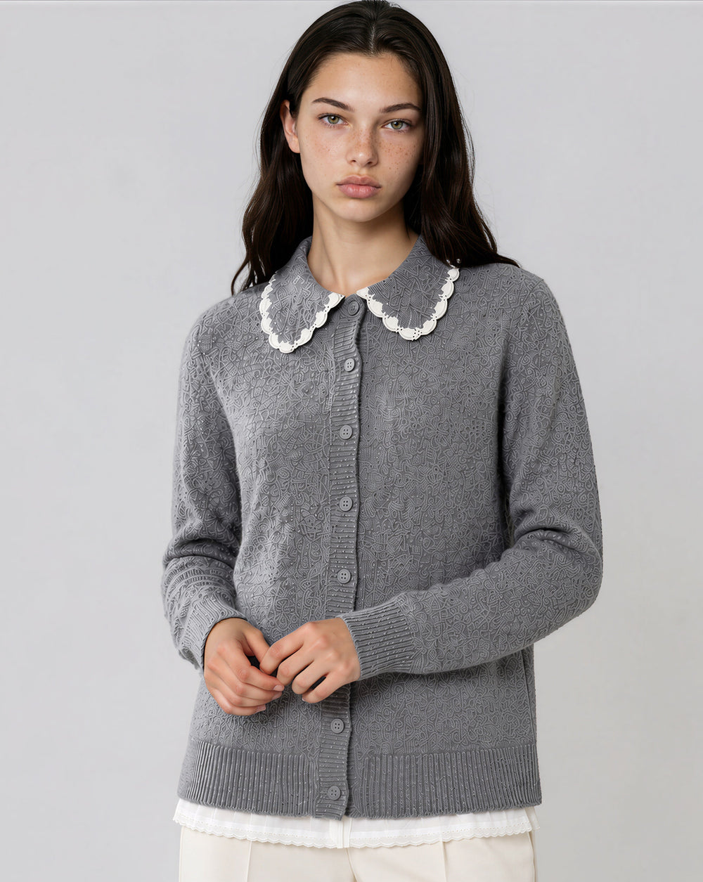 A woman modeling a gray knit cardigan sweater with a white scalloped Peter Pan collar, shown against a plain light gray studio background.