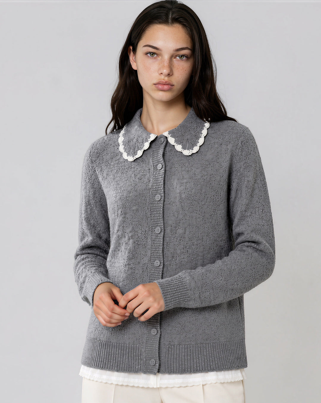 A woman modeling a gray knit cardigan sweater with a white scalloped Peter Pan collar, shown against a plain light gray studio background.