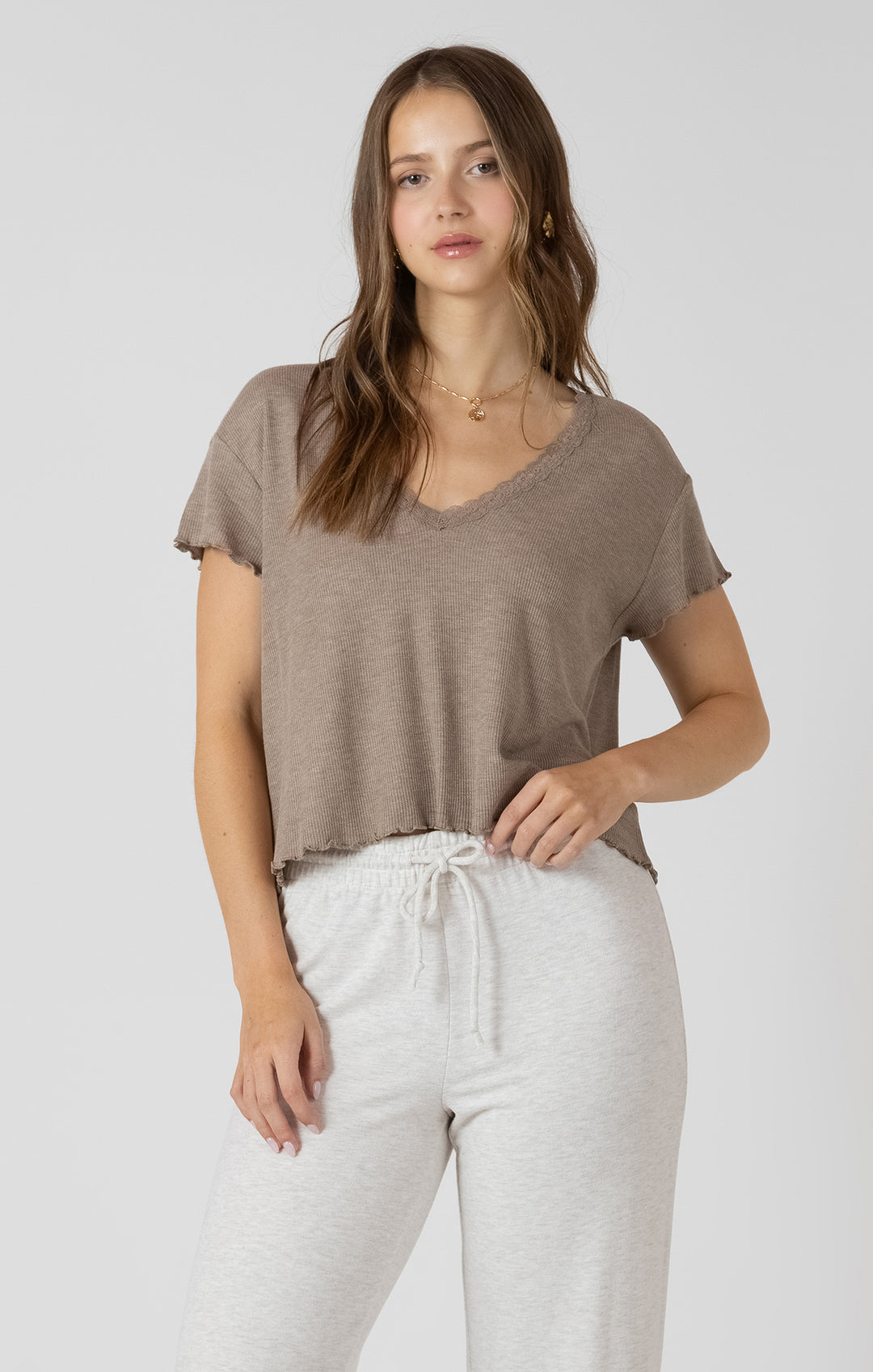 Woman wearing a brown t-shirt and white pants on a plain background