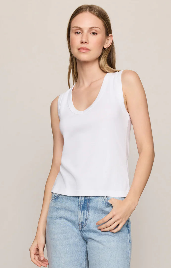 Woman wearing a white sleeveless top and light blue jeans on a beige background