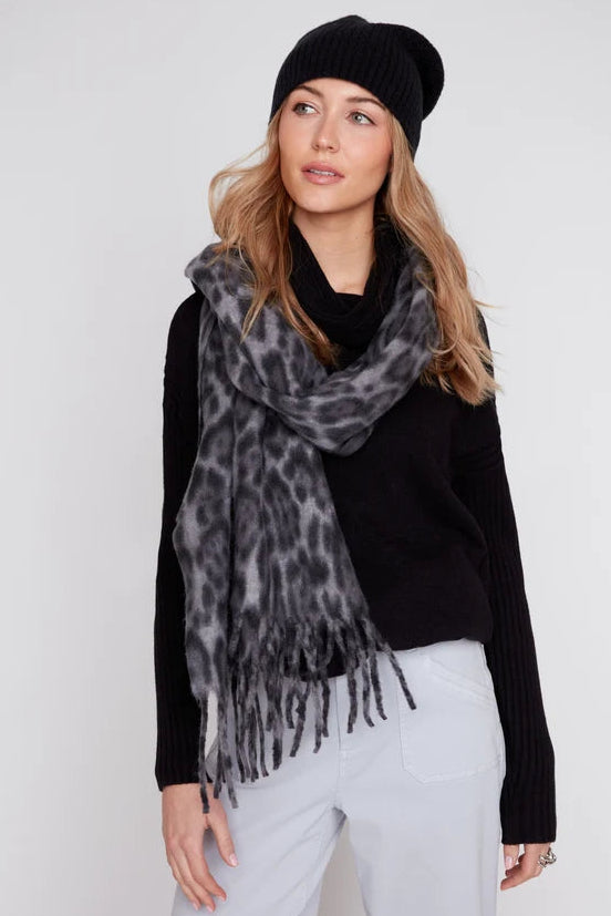 Woman wearing a black knit sweater, white pants, and a patterned scarf with a plain background