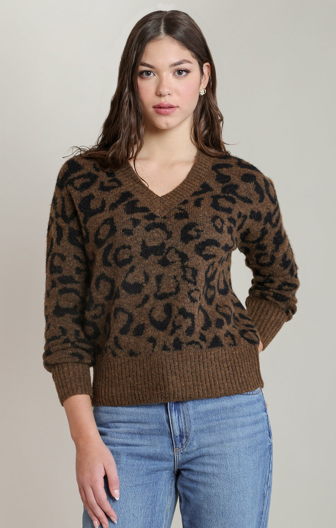 Woman wearing a brown leopard print sweater and blue jeans on a plain background