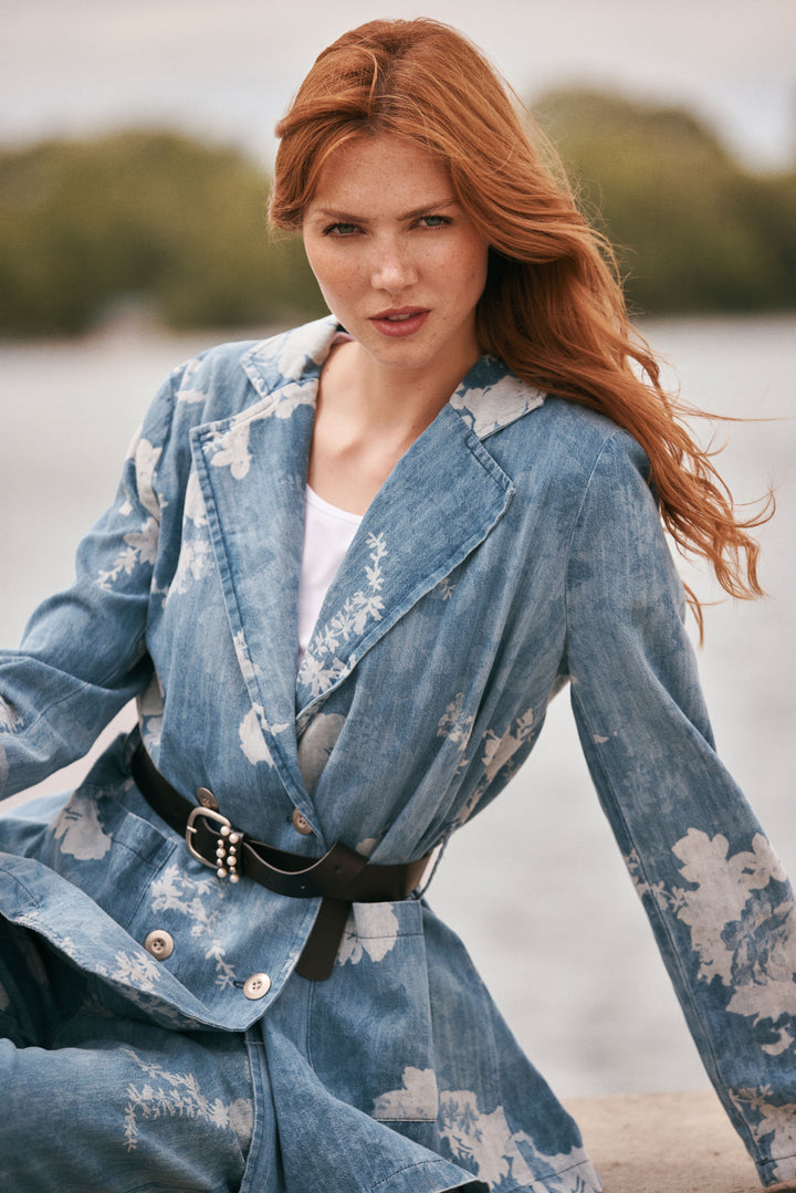 Woman wearing a blue floral dress sitting by a body of water.