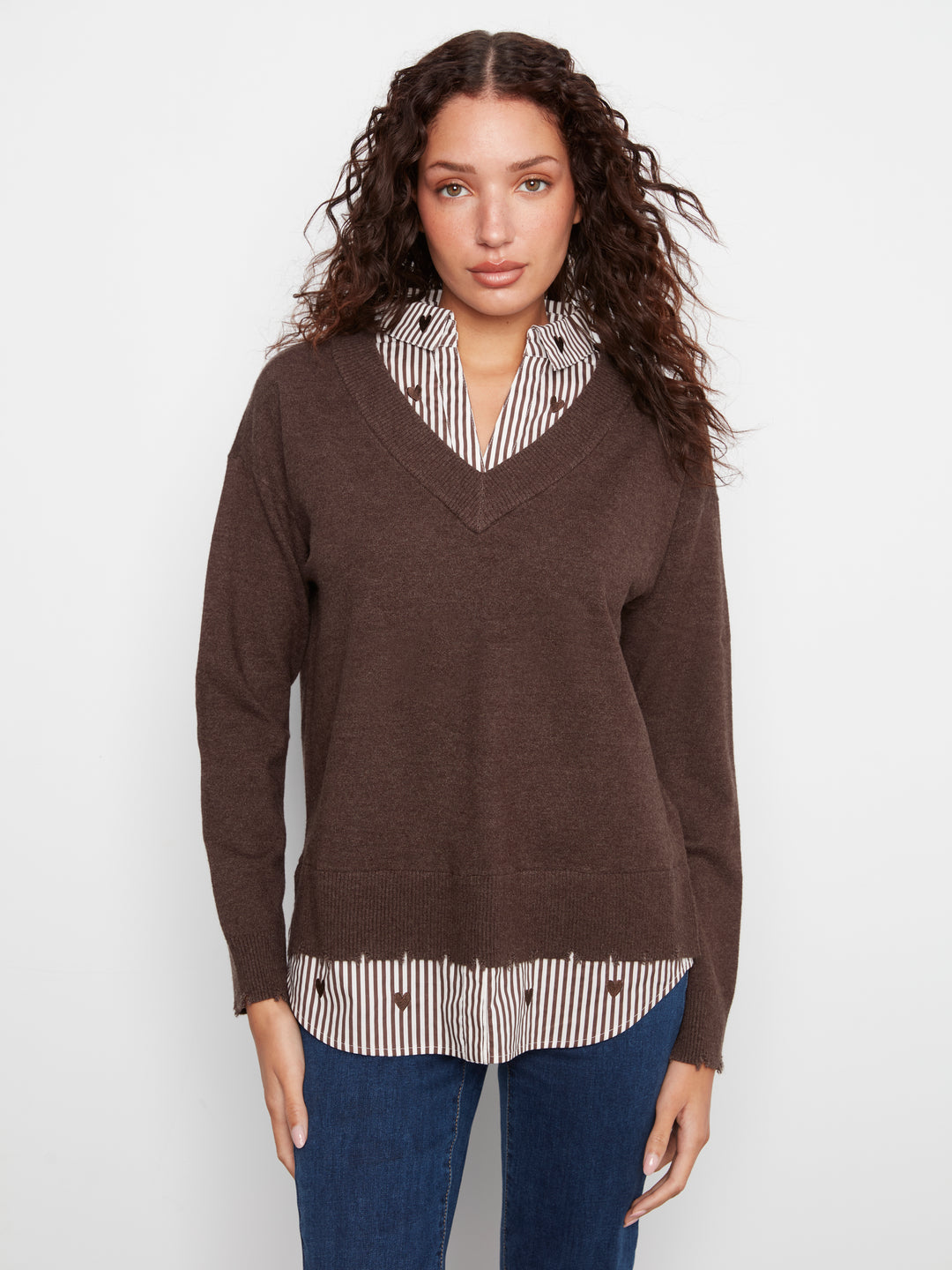 Woman wearing a brown sweater over a striped shirt with a white background