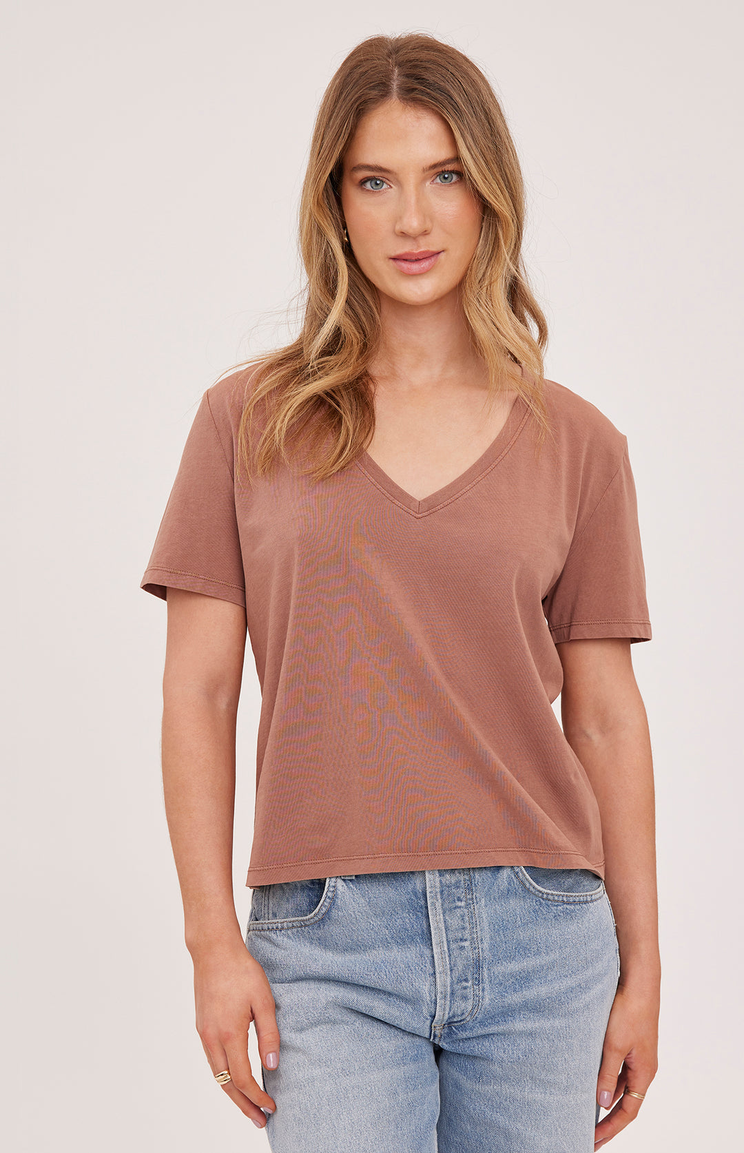 Woman wearing a brown t-shirt and blue jeans against a plain background