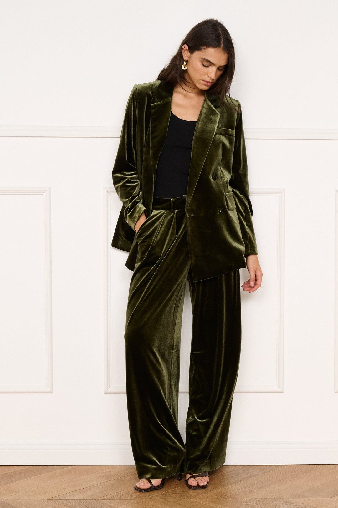 Woman wearing a green velvet suit standing against a white wall.