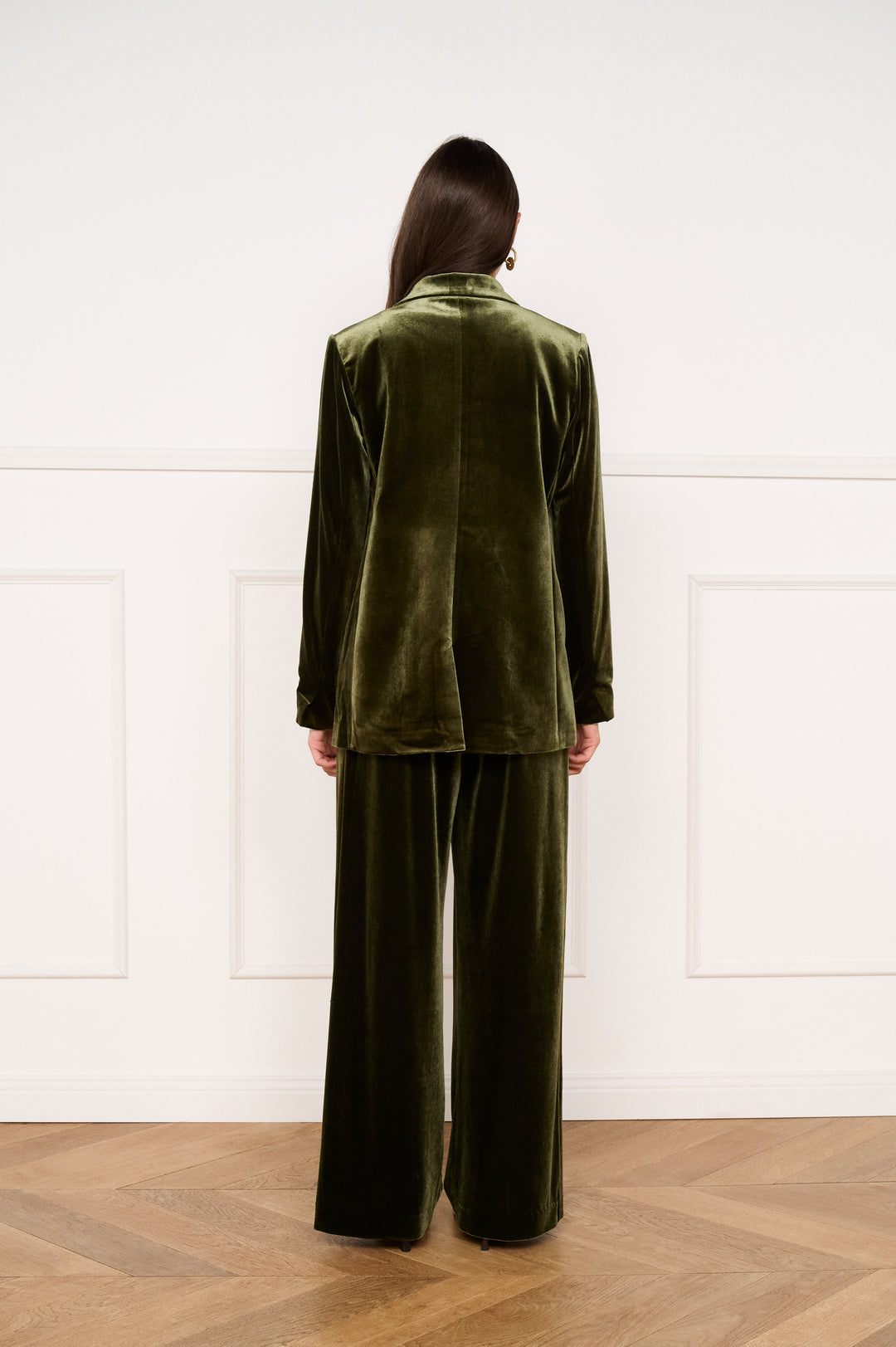 Person wearing a green velvet suit standing against a white paneled wall.