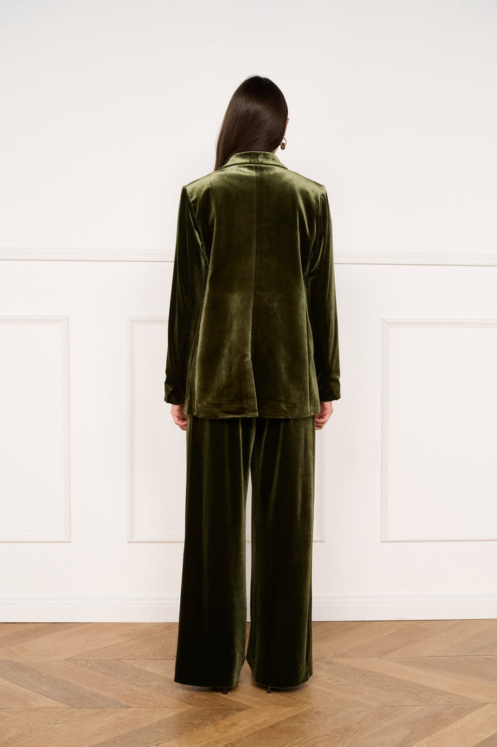 Person wearing a green velvet suit standing against a white paneled wall.