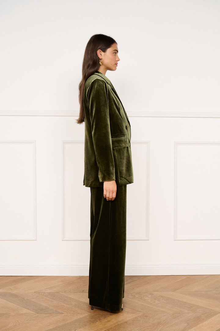 Woman wearing a green velvet outfit standing against a white wall.