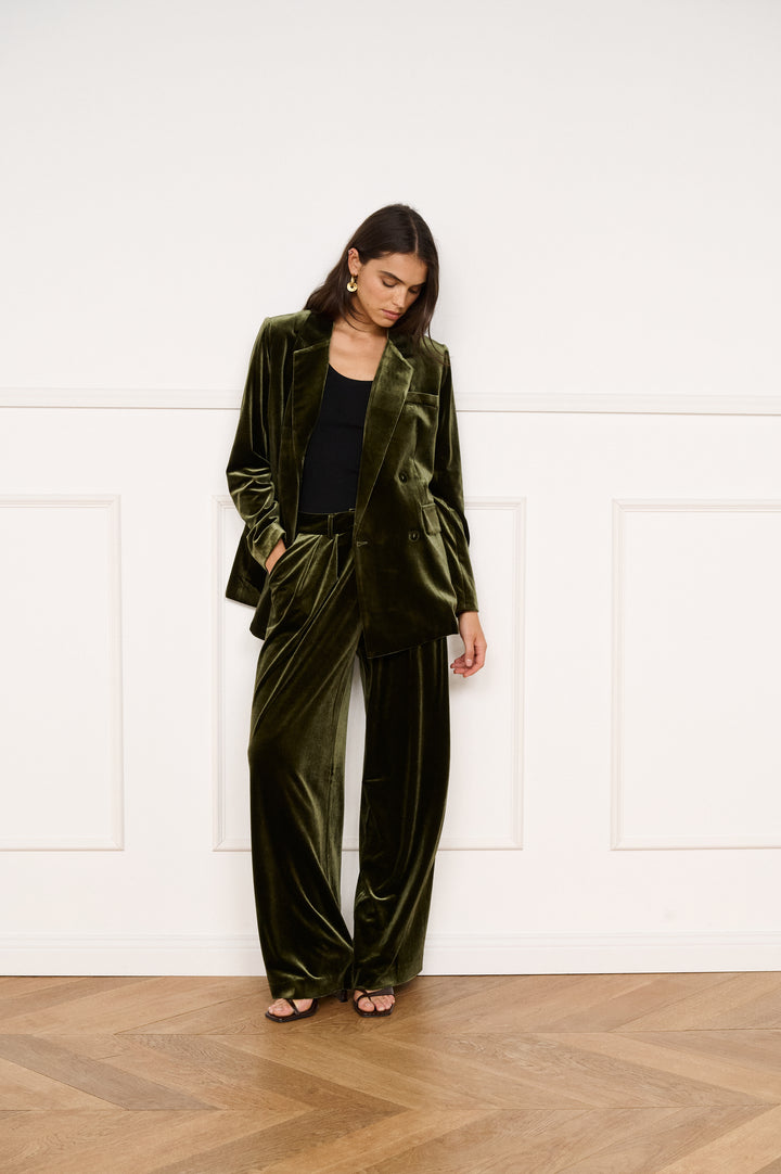 Woman wearing a green velvet suit standing against a white wall.