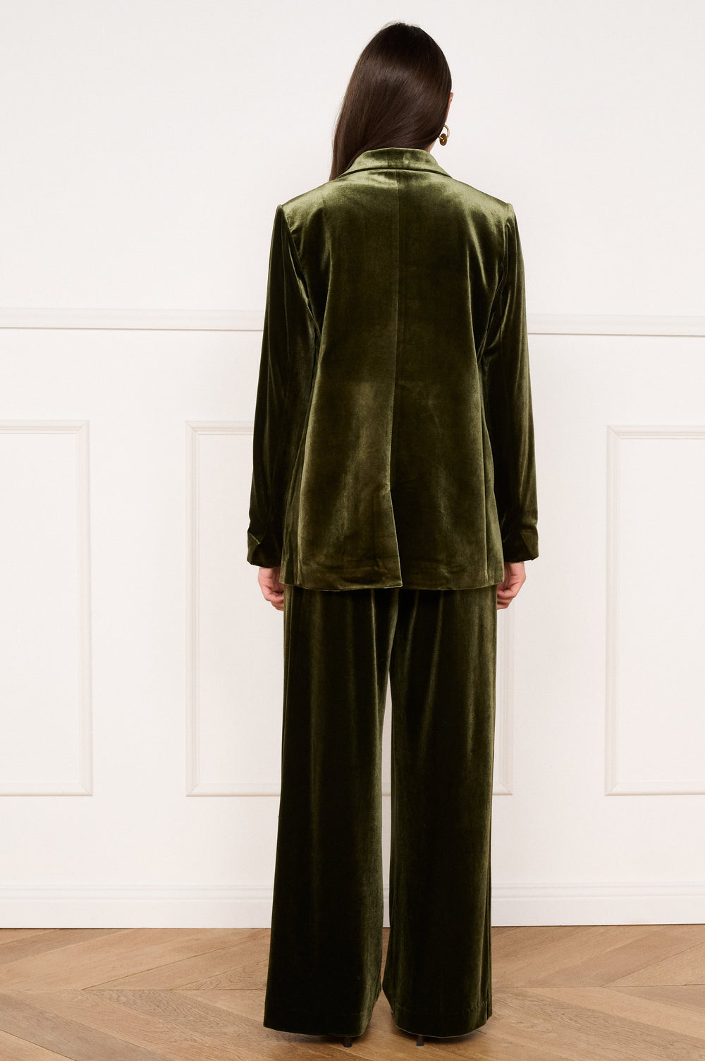 Person wearing a green velvet suit standing against a white paneled wall.