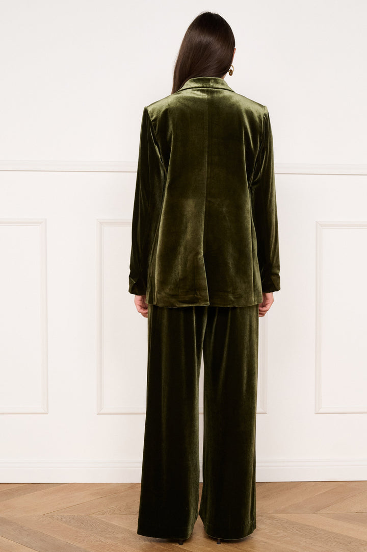 Person wearing a green velvet suit standing against a white paneled wall.