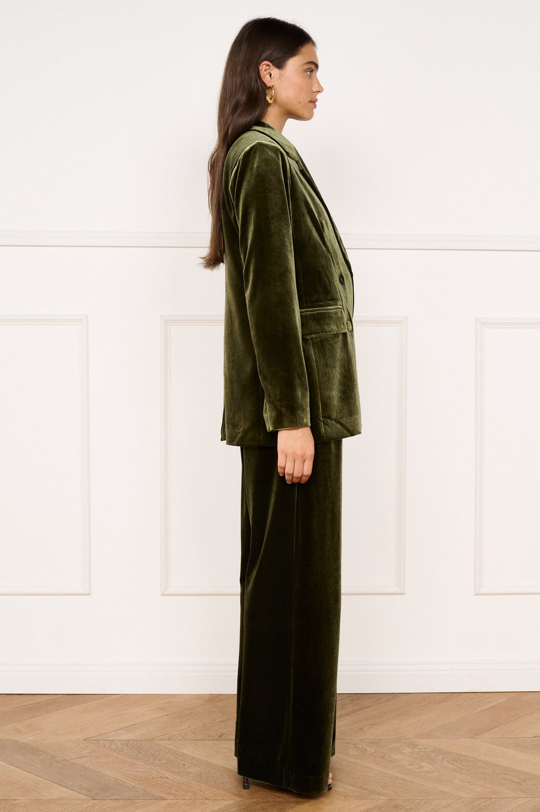 Woman wearing a green velvet outfit standing against a white wall.