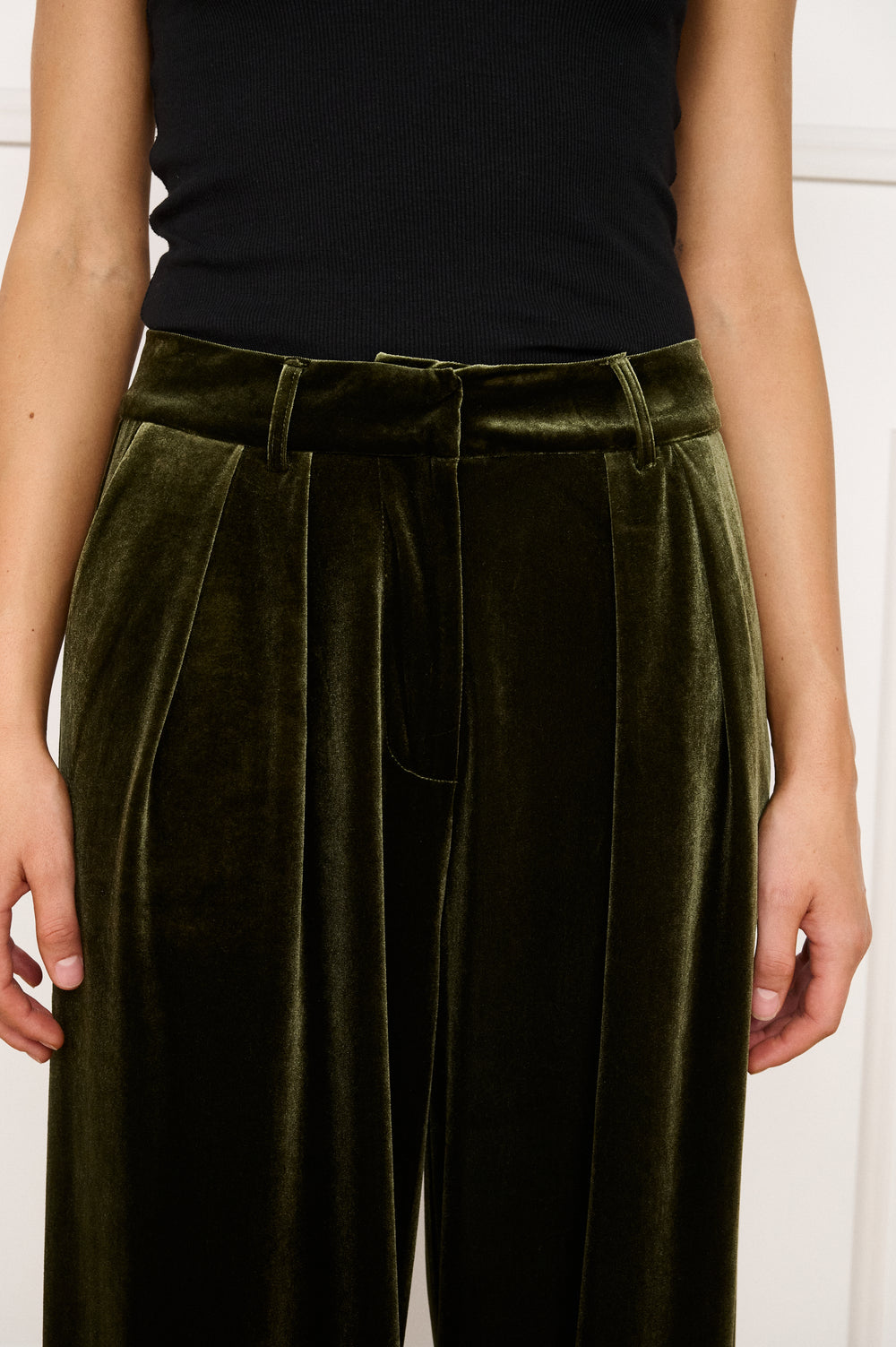 Person wearing olive green velvet pants with a black top against a white background
