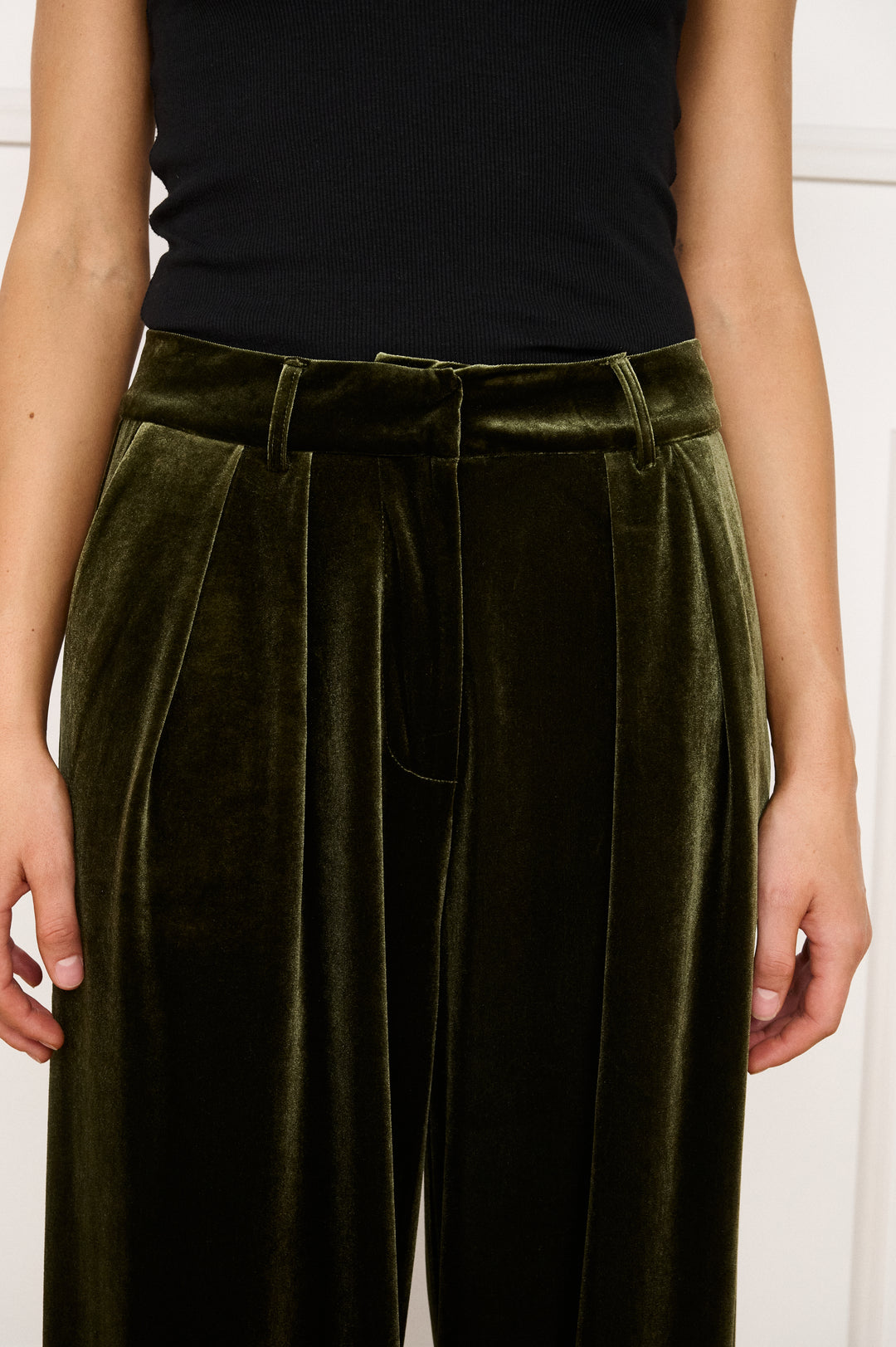 Person wearing olive green velvet pants with a black top against a white background