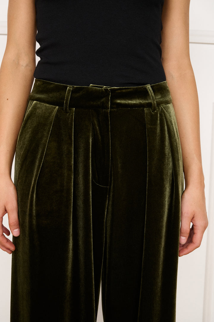Person wearing olive green velvet pants with a black top against a white background