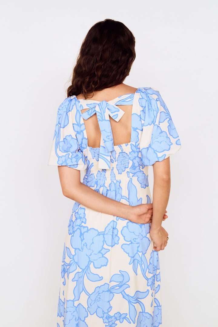 Woman wearing a blue floral dress with cut-out back design on a white background
