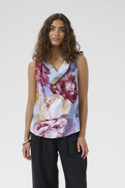Woman wearing a floral sleeveless top and black pants on a white background