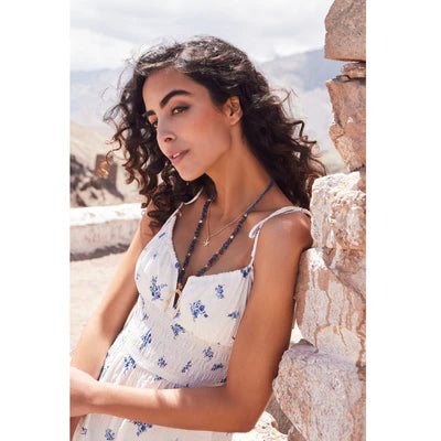 Woman in a white floral dress sitting against a stone wall with a scenic background