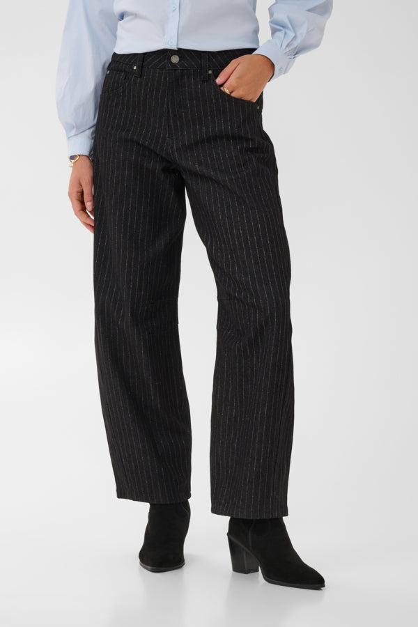 A person wearing black pinstriped trousers with a light blue button-up shirt and black ankle boots, shown from the waist down against a clean white studio background.