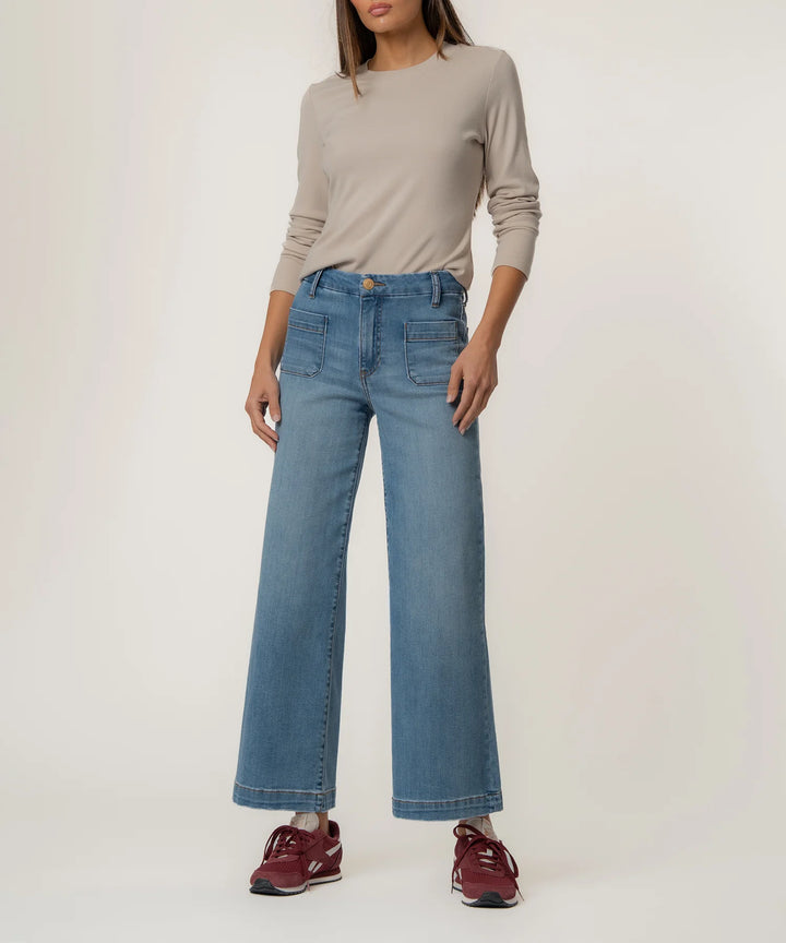 Person wearing a beige long-sleeve top and blue jeans on a white background