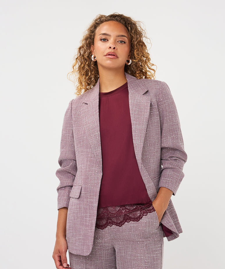 A model wearing a matching lavender-gray textured blazer and trousers set with a burgundy top, photographed against a clean light gray studio background.