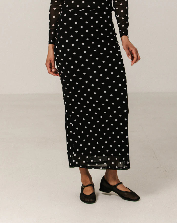 Person wearing a black dress with white polka dots on a plain background