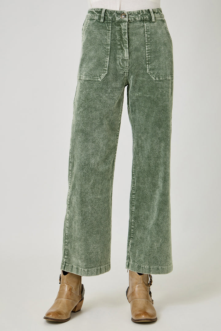 A pair of wide-leg cropped pants in a washed sage green corduroy fabric, styled with brown leather ankle boots against a light gray studio background.