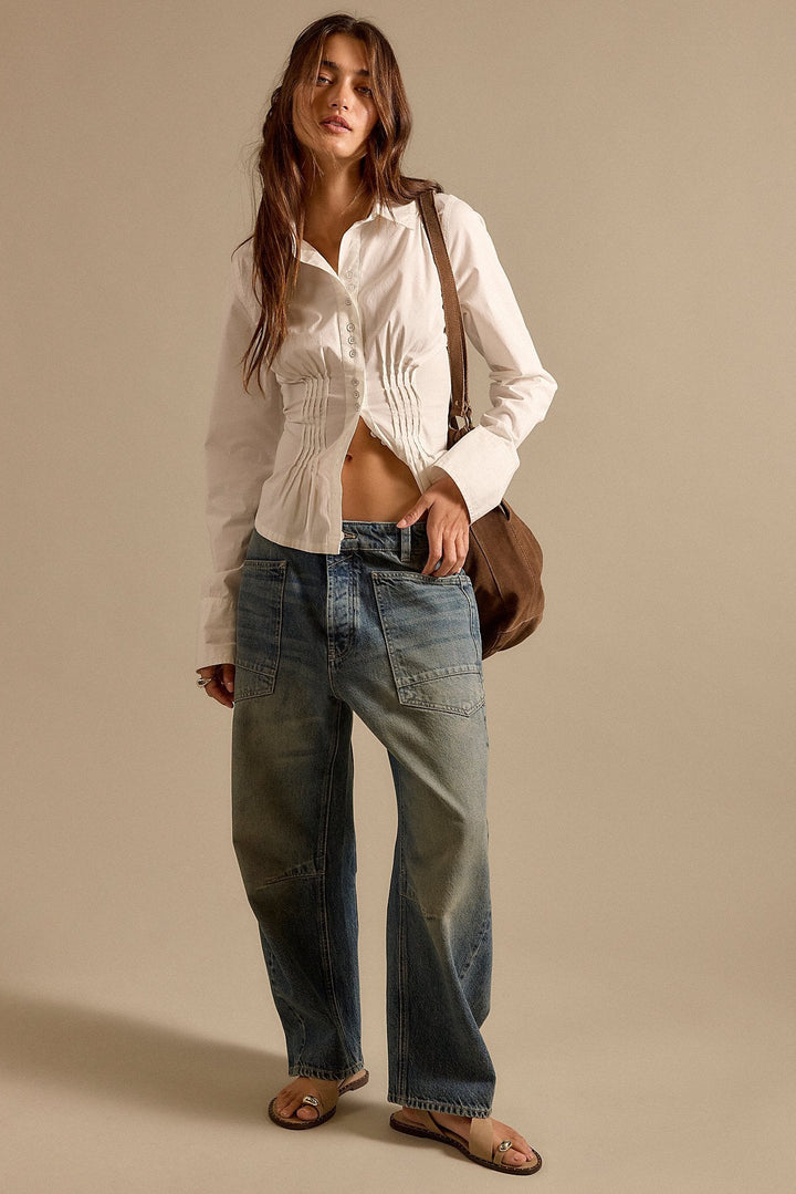 Woman wearing a white shirt and blue jeans with a brown bag on a beige background