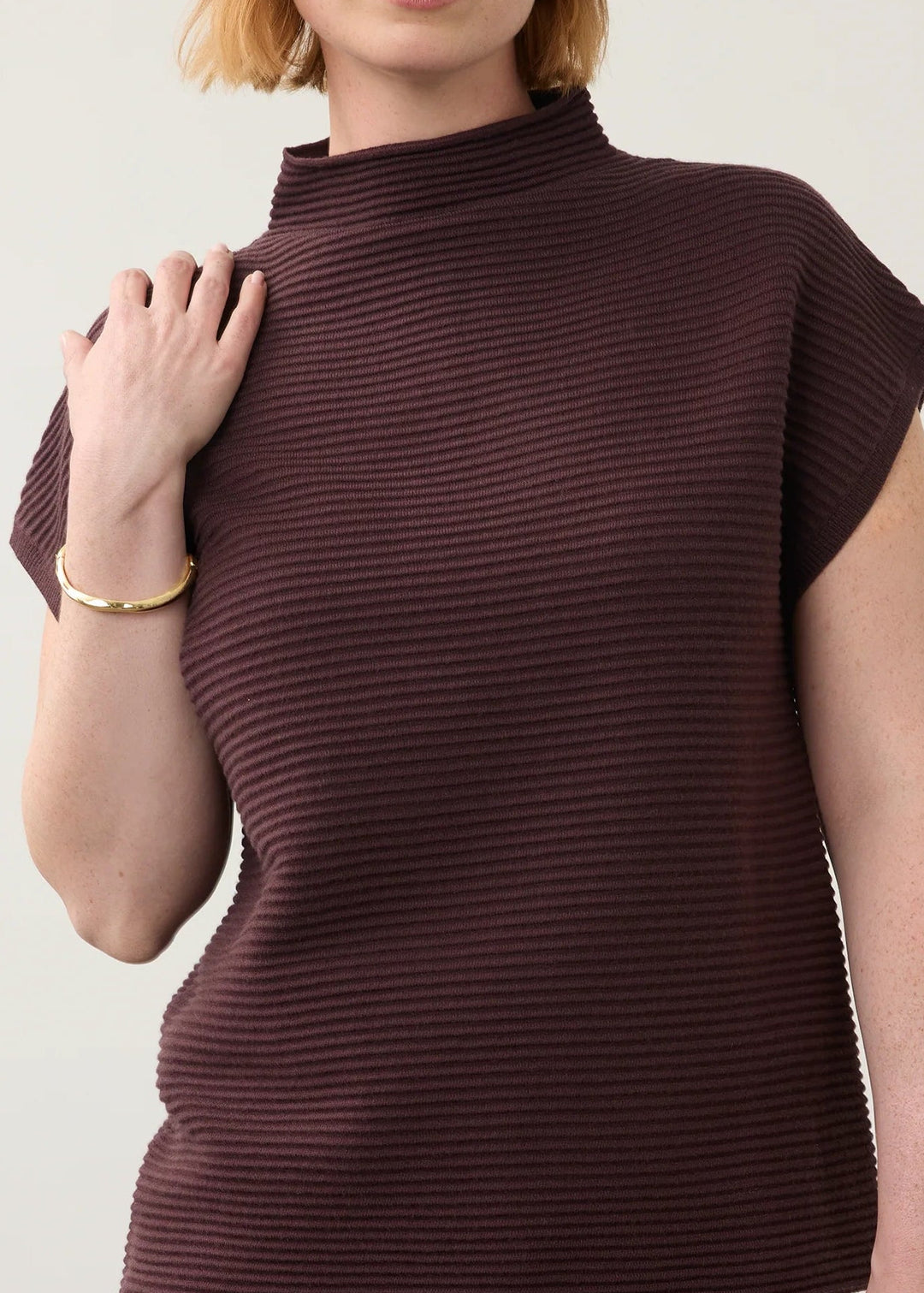 A woman modeling a ribbed knit mock-neck top in deep burgundy with matching trousers, set against a plain light gray studio background.