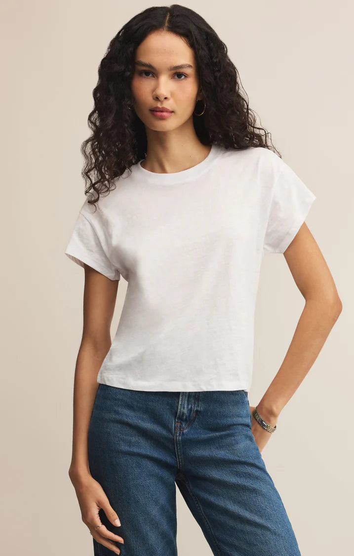 Woman wearing a white t-shirt and blue jeans against a beige background