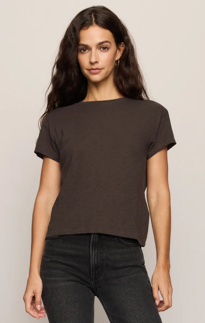 Woman wearing a black t-shirt and dark jeans against a plain background